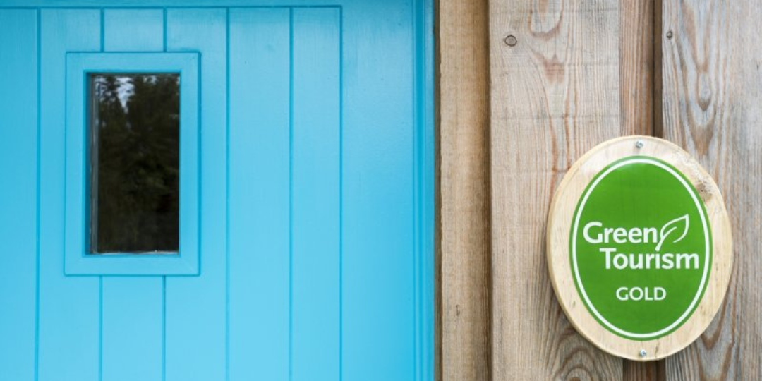 Blue door with Green Tourism plaque on a wood background